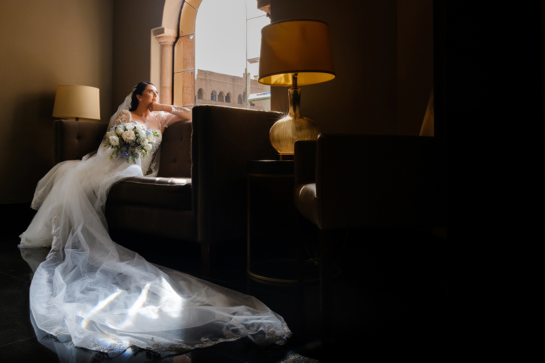 Una novia con vestido blanco sentada frente a una ventana el día de su boda.